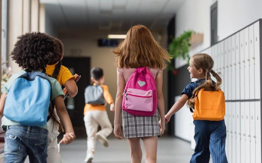 Back view of schoolchildren with backpacks walking in corridor of school.