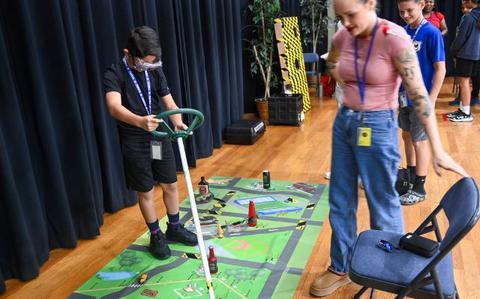 Photo Of U.S. Army Sgt. Emma Graves, U.S. Army Garrison Army Substance Abuse Program intern, observes a student simulating driving while wearing impairment googles during Red Ribbon week, at Ryukyu Middle School, Okinawa, Japan.