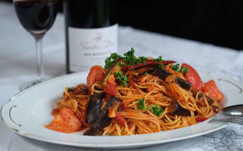 Photo Of pasta pomodoro, a glass of red wine, and a bottle of red wine on the table.
