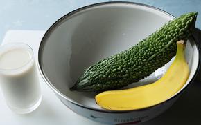 A goya and a banana in a bowl. A glass of milk is beside it.