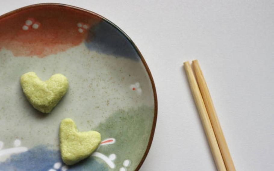 chopsticks and two heart-shaped wasabi on a dish are on a table.