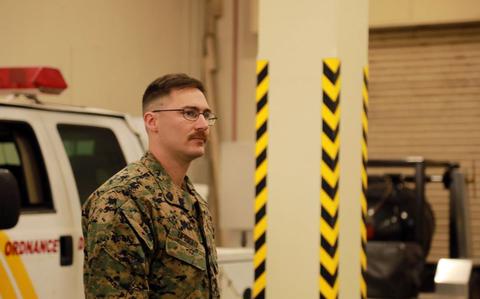 Photo Of Sgt. Joshua Upright gives a briefing. A vehicle can be seen behind him.