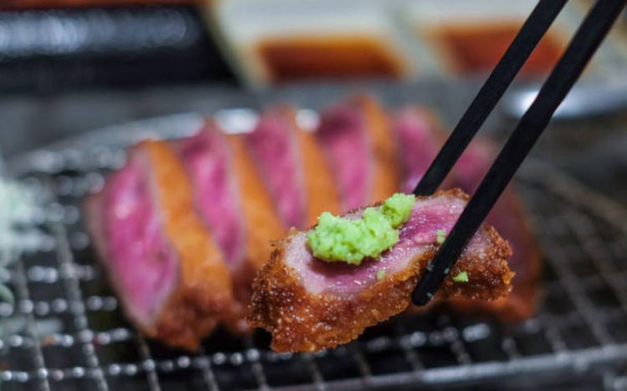 meat is cooked on a wire net and one of them is picked up with chopsticks and wasabi is on it.