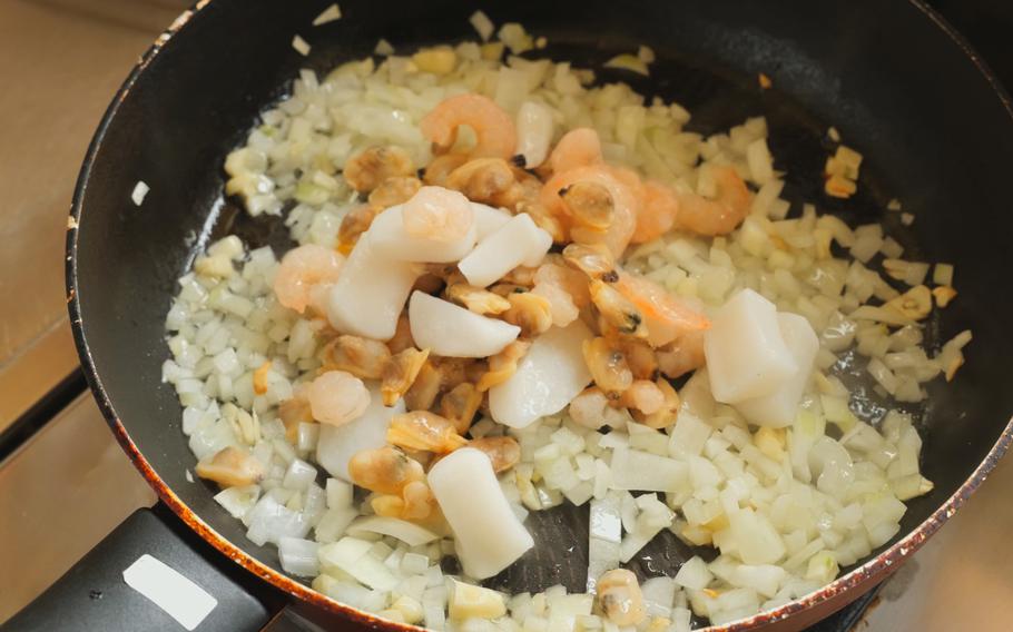 Pour olive oil into a pan and fry chopped garlic first, to be followed by chopped onion, and frozen mixed seafood.