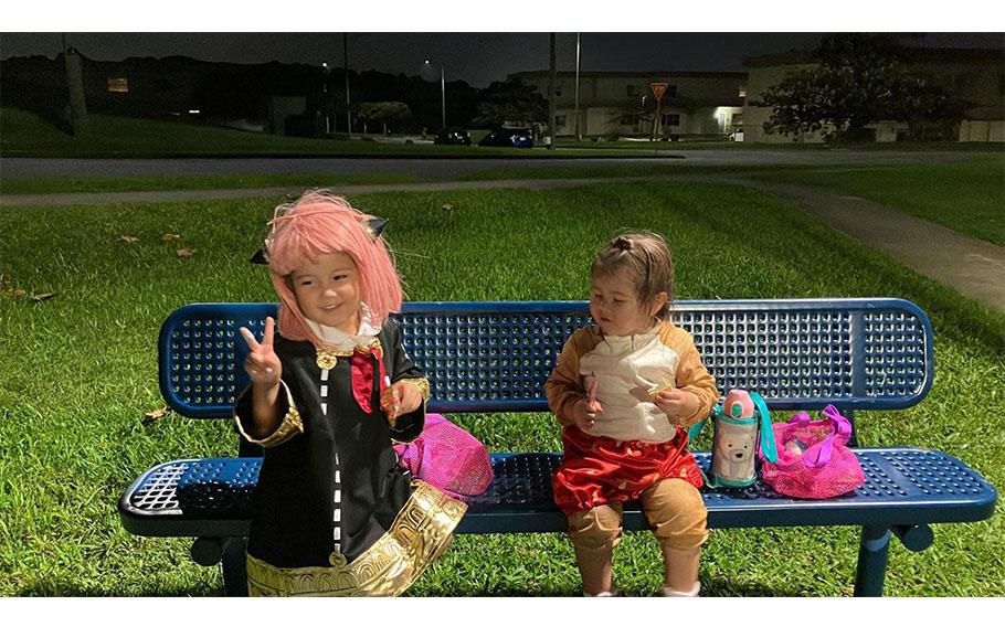 two kids with costumes are having a seat on a bench.