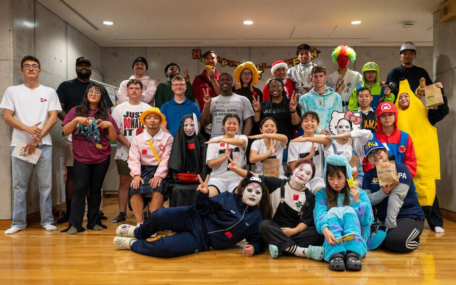 18th Wing volunteers and Kadena Language Institute students pose for a group photo after a Halloween-themed event at Kadena Town. About thirty people are in the photo.