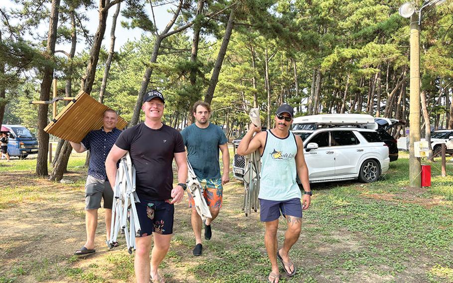 Four men are carrying camping goods.