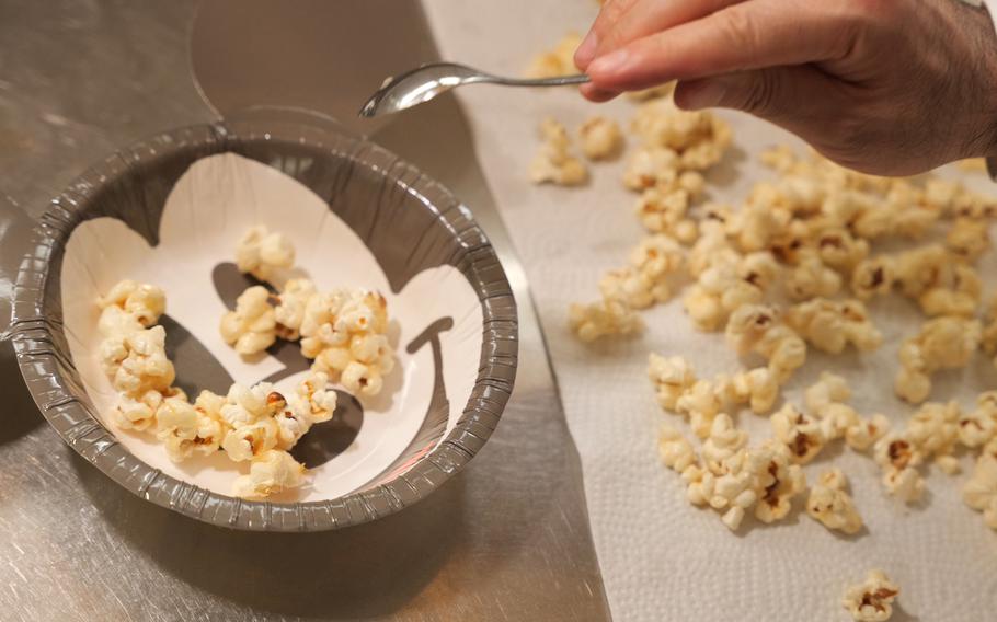 Shoji is putting popcorn on a bowl with spoon.