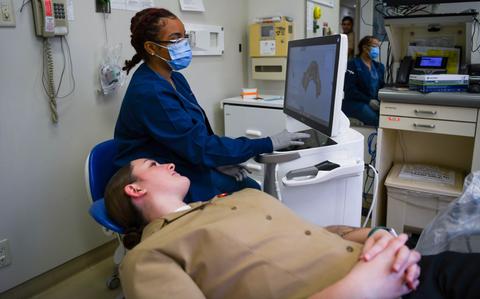 Photo Of U.S. Air Force Airman 1st Class Aliyah Parker, back, 18th Dental Squadron orthodontic technician, utilizes a Computer Aided Design and Computer Aided Manufacturing machine on U.S. Navy Hospital Corpsman 3rd Class Mackenzi Barksdale, front, 3rd Dental Battalion dental technician, to make a 3D model of their own mouth during the 67th Tri-Service Dental Conference at Kadena Air Base, Japan, March 13, 2024.