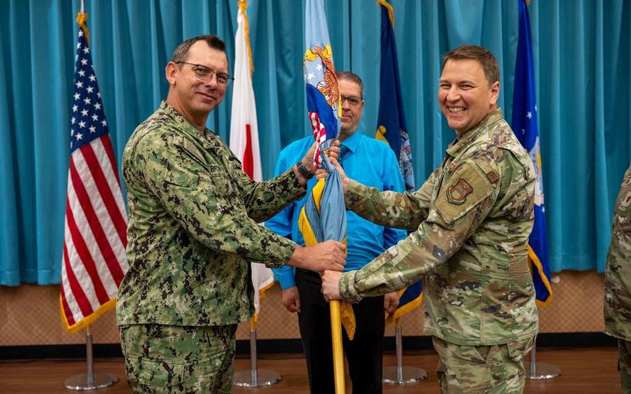U.S. Navy Capt. Patrick Brown, Defense Logistics Agency Indo-Pacific commander, left, passes the guidon to U.S. Air Force Maj. Dominic Baker, DLA Energy Okinawa incoming commander, right, during a change of command ceremony.
