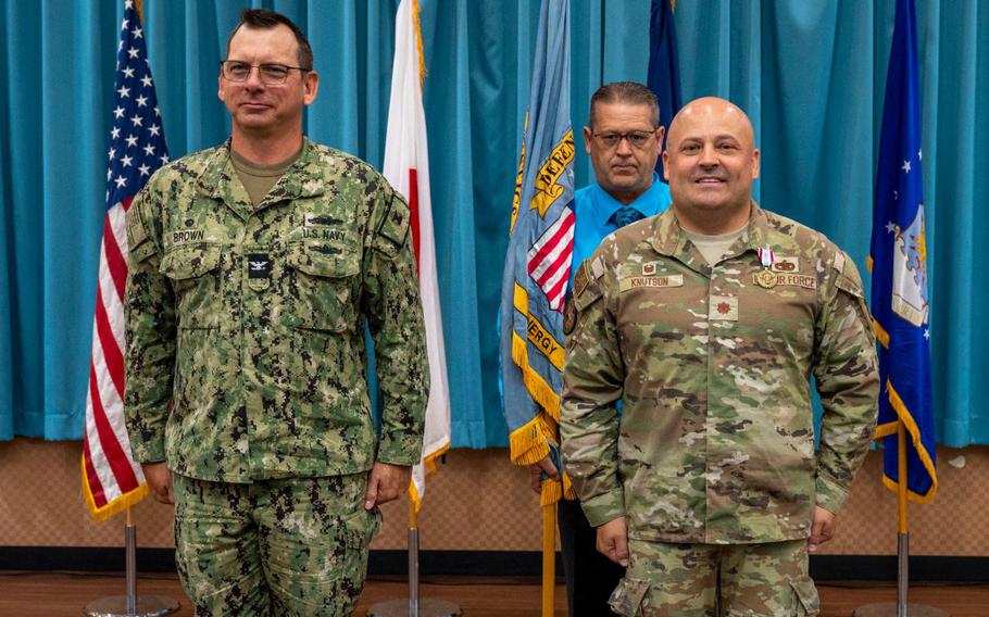 U.S. Navy Capt. Patrick Brown, Defense Logistics Agency Indo-Pacific commander, left, prepares to receive the guidon from U.S. Air Force Maj. Kevin Knutson, DLA Energy Okinawa outgoing commander, right, during a change of command ceremony.