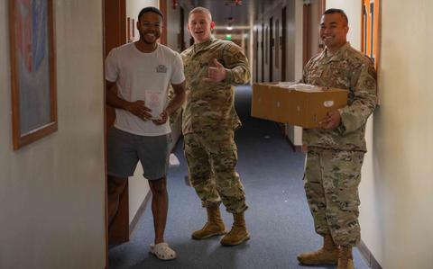 Photo Of A Kadena dorm resident receives a bag of cookies from U.S. Air Force Master Sgt. Sean Paulino, 18th Medical Group first sergeant, center, and Tech Sgt. Adrian Thompson, 718th Civil Engineer Squadron airman dorm leader, during the annual cookie drive at Kadena Air Base, Japan, Dec. 12, 2024.