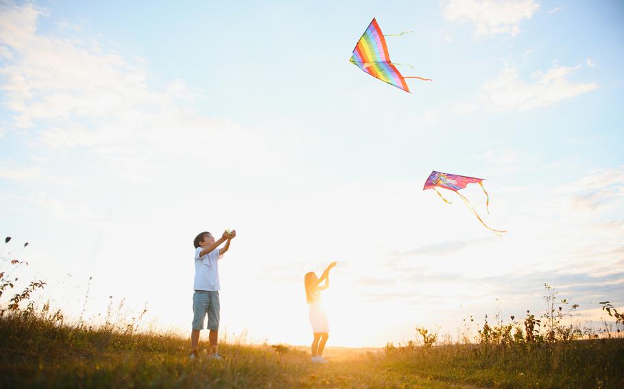 Children launch a kite in the field at sunset.